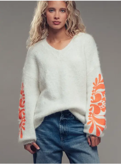 Person wearing a white sweater with orange floral patterns on a gray background